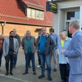 Eine Gruppe von Männern steht zusammen. Die Personen sind unterschiedlich gekleidet und scheinen sich zu unterhalten.