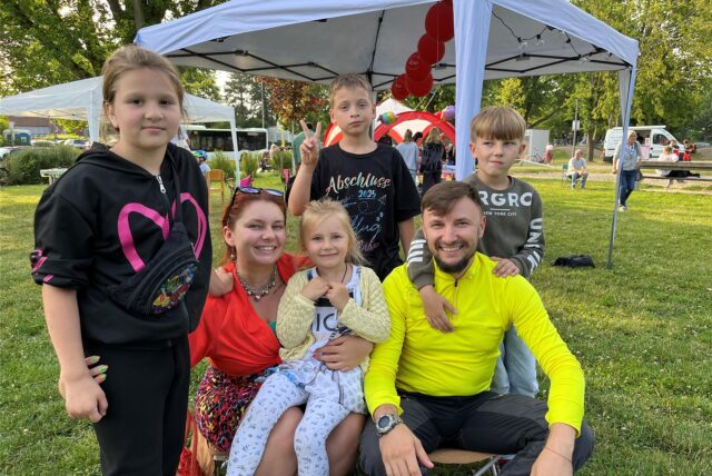 Eltern sitzen mit ihren Kindern auf der Wiese.