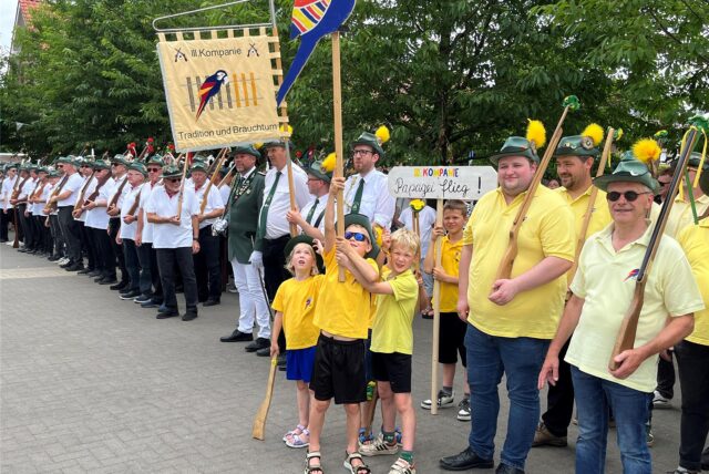 Kinder halten ein Banner hoch mit einem Papagei bestickt.