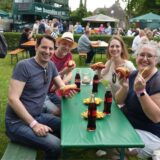 Menschen sitzen an einem Tisch. Vor sich haben sie Getränke, Bratwurst und Pommes Frites.