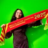 Volontärin Rosi Taslima Azam steht mit einem Hansetag-Schal vor einer grünen Wand.