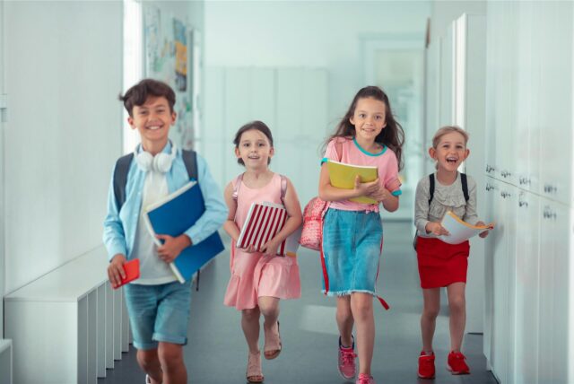 Fröhliche Kinder in sommerlicher Kleidung beim Verlassen des Schulgebäudes, weil sie Hitzefrei haben.