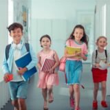 Fröhliche Kinder in sommerlicher Kleidung beim Verlassen des Schulgebäudes, weil sie Hitzefrei haben.