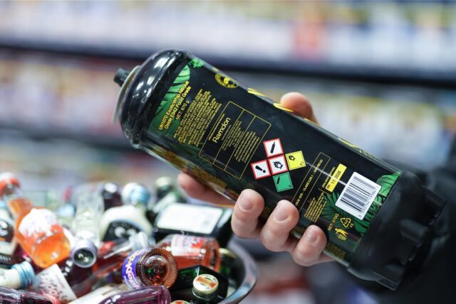 Ein Mitarbeiter hält eine Dose Lachgas am Tresen eines Kiosks in der Hand.