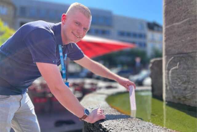 RN-Reporter Johannes Wenzel hält ein Thermometer in den Brunnen am Markt in Castrop-Rauxel.
