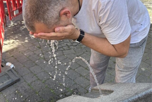 Ein Mann spritzt sich an einem Trinkbrunnen Wasser ins Gesicht.