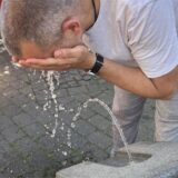 Ein Mann spritzt sich an einem Trinkbrunnen Wasser ins Gesicht.
