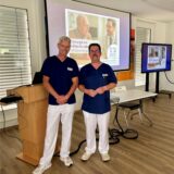 Dr. Christian Kühne, Chefarzt für Chirurgie am EvK Castrop-Rauxel, und Olaf Trenke, Oberarzt der Klinik für Anästhesie, stehen vor einer Leinwand, auf der eine Präsentation zu sehen ist.