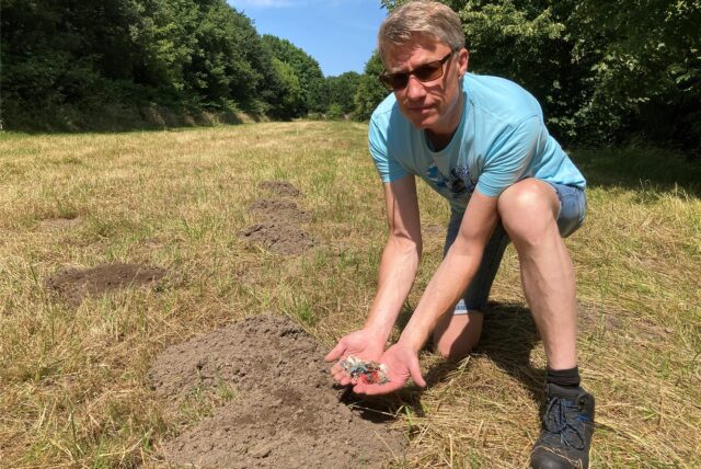 Mann zeigt Plastikmüll auf Wiese
