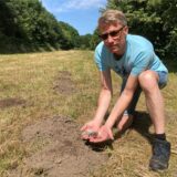 Mann zeigt Plastikmüll auf Wiese