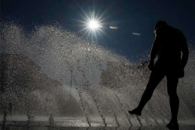 Ein Mann kühlt sich an einem Brunnen im Wasser ab.