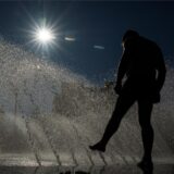 Ein Mann kühlt sich an einem Brunnen im Wasser ab.