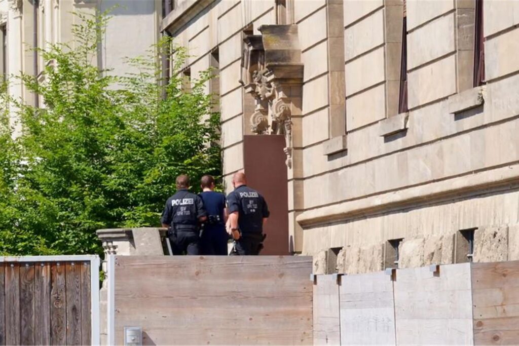 Das Standbild aus einem Video zeigt, wie Polizeibeamte den Verdächtigen, der am Dienstag beim Stromversorger Überlandwerk Rhön in Mellrichstadt Kollegen mit einem Messer angegriffen, verletzt und eine tödlich verletzt haben soll, ins Gerichtsgebäude bringen. Das Standbild aus einem Video zeigt, wie Polizeibeamte den Verdächtigen, der am Dienstag beim Stromversorger Überlandwerk Rhön in Mellrichstadt Kollegen mit einem Messer angegriffen, verletzt und eine tödlich verletzt haben soll, ins Gerichtsgebäude bringen.