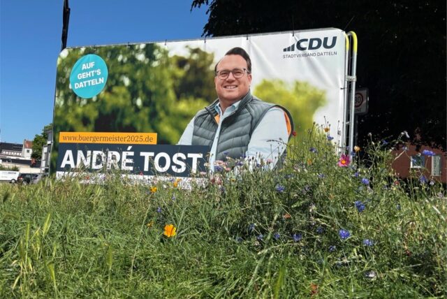 Ein Wahlplakat steht auf einer Wiese. es zeigt den CDU-Kandidaten für Datteln André Tost.