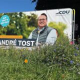 Ein Wahlplakat steht auf einer Wiese. es zeigt den CDU-Kandidaten für Datteln André Tost.