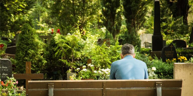 Mann sitzt auf dem Friedhof auf einer Bank