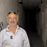 Ein Mann mit einer Sonnenbrille im Haar und einem karierten Hemd steht in einem dunklen Gang.