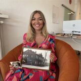 Leonie Becker sitzt mit alten Bildern des Hauses Molkereistraße 1 in einem Sessel in ihren Geschäftsräumen.