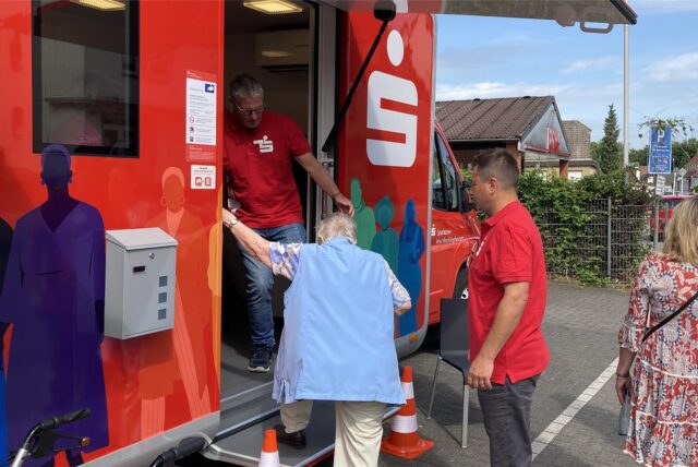 Eine Frau steigt in den Sparkassenbus ein, zwei Männer helfen ihr.