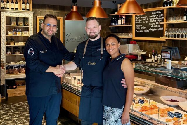 Daniel Georgiev (l.) schüttelt im Delikatessenladen die Hand von Milan Makovy, an dessen Seite Ehefrau Jennifer Adu-Makovy steht.
