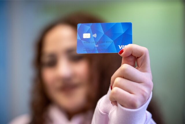 Frau im Hintergrund zeigt blaue Bezahlkarte für Geflüchtete.