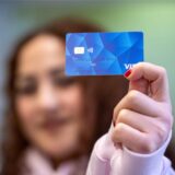 Frau im Hintergrund zeigt blaue Bezahlkarte für Geflüchtete.