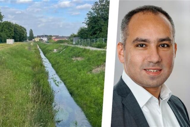 Eine malerische Landschaft zeigt einen kleinen Flusslauf, der von üppigem Grün und Bäumen gesäumt ist. Im Hintergrund sind Wohnhäuser und ein bewölkter Himmel sichtbar. Daneben ist das Foto eines Mannes zu sehen, der ein weißes Hemd und eine graue Anzugsjacke trägt.