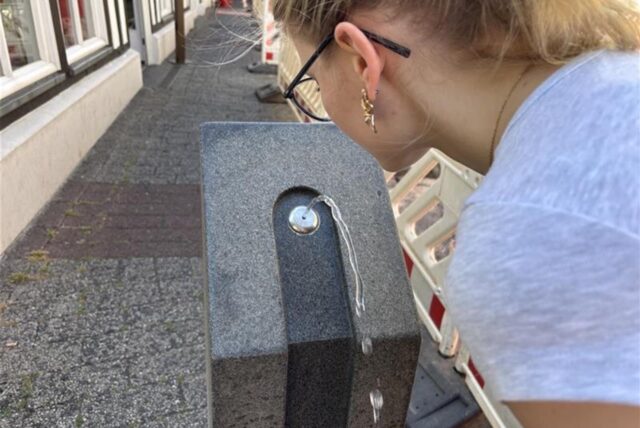 Eine Frau trinkt an einem öffentlichen zugänglichen Brunnen.