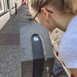 Eine Frau trinkt an einem öffentlichen zugänglichen Brunnen.