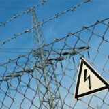 Ein Gefahrenschild für Elektrizität ist vor einer Stromtrasse zu sehen.