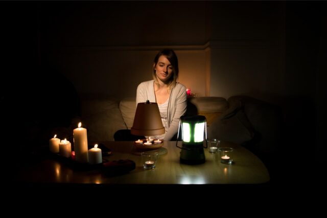 Eine Frau sitzt während eines Stromausfalls bei Kerzenlicht auf ihrer Couch.