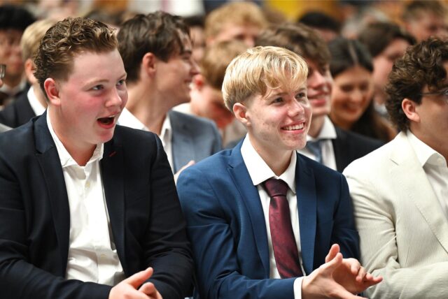 Schüler sitzen mit festlicher Kleidung in der Sporthalle des Gymnasium Petrinum in Recklinghausen und applaudieren.
