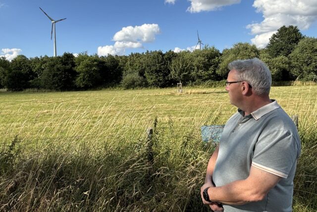 Andreas Lamberty vor einem Feld in Ellinghausen. Im Hintergrund die Windräder der „EllWira“-Anlage.