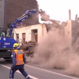 THW-Einsatzkraft vor einem Abrissbagger im Staub der Bauruine.
