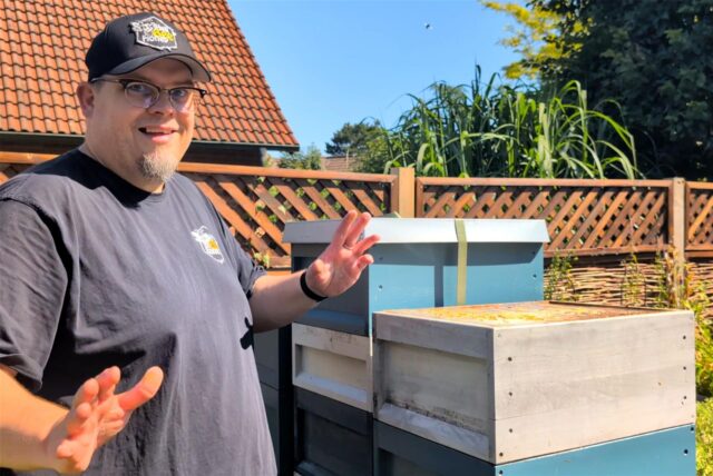 Imker Patrick Kramer steht in seinem Garten vor seinen Bienenvölkern.