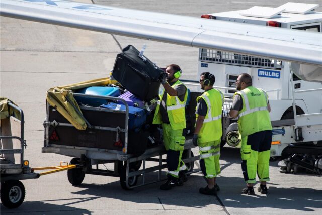 Mitarbeiter eines deutschen Flughafens verladen Koffer in ein Flugzeug.
