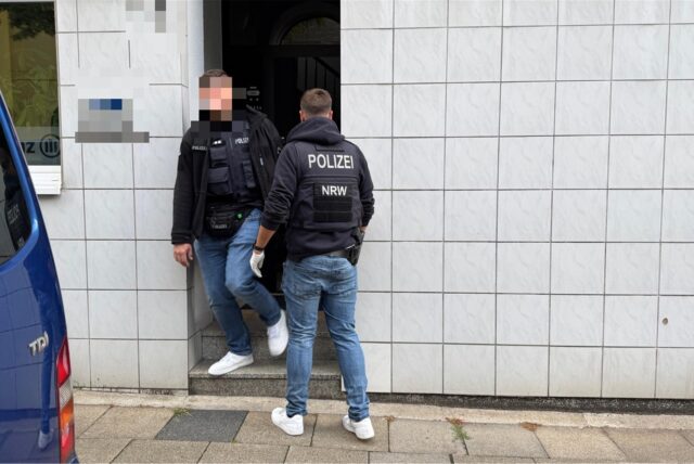 Zwei Polizisten stehen in einem Hauseingang bei einer Razzia in NRW.