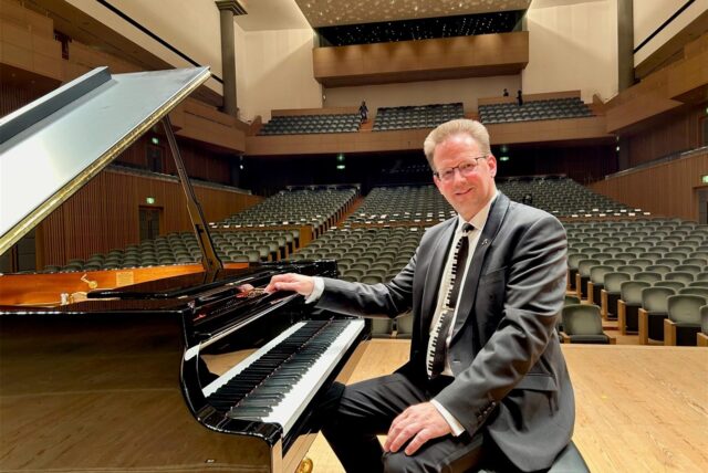 Der Marler Pianist Volker Zwetzschke kurz vor einem Auftritt in Japan. Er sitzt auf einer Bühne am Flügel. Die Publikumsränge sind leer.