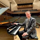 Der Marler Pianist Volker Zwetzschke kurz vor einem Auftritt in Japan. Er sitzt auf einer Bühne am Flügel. Die Publikumsränge sind leer.