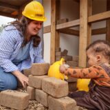 Jana Eckei sitzt mit ihrem Sohn Mediaabar auf der Spielbaustelle des Guts Königsmühle und spielt mit Bauhelmen und Spielzeug-Ziegelsteinen