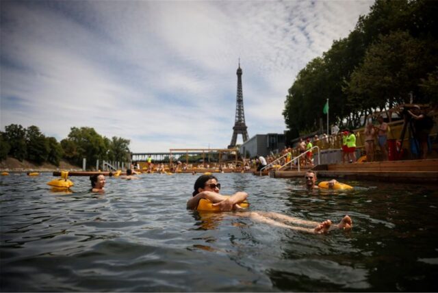 Menschen genießen das Wasser an der sicheren Badestelle Grenelle an der Seine in Paris. Im Hintergrund ist der Eifelturm zu sehen.