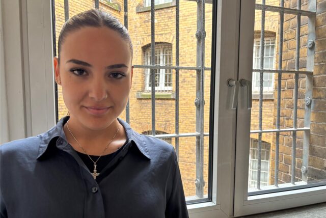 Garyfalia Bania steht vor einem vergitterten Fenster der JVA Dortmund.