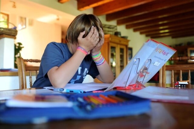 Ein Kind sitzt vor einem Buch und hat die Hände vor das Gesicht geschlagen.