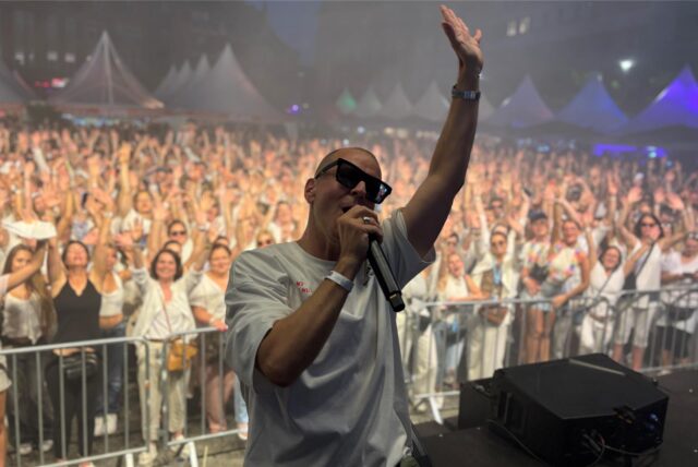 DJ Moguai mit einem Mikro in der Hand vor einer feiernden Menge.