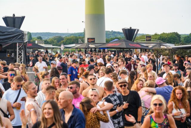 Junge Menschen auf der Veranstaltungsfläche des eintägigen Techno-Festivals Querfeldein unterhalb eines Windrads in Recklinghausen-Essel.