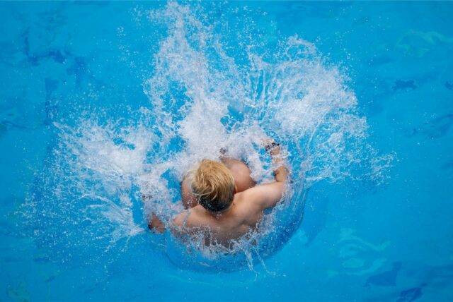 Ein Junge macht eine Arschbombe in ein Schwimmbecken