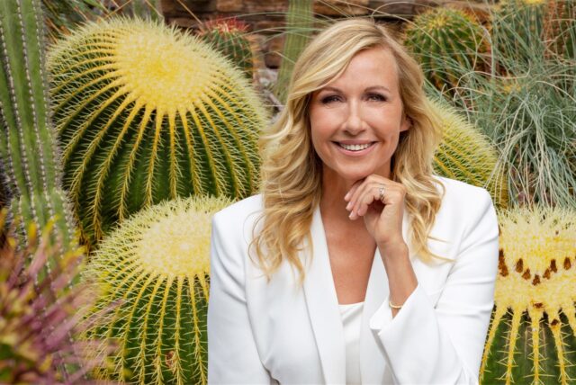 ZDF-Fernsehgarten-Moderatorin Andrea Kiewel (Kiwi) sitzt in einem weißen Blazer vor Kakteen.