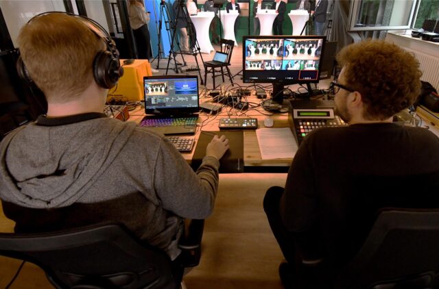 Zwei Männer sitzen in einem Videostudio und schauen auf Bildschirme.