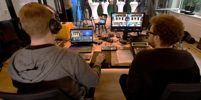 Zwei Männer sitzen in einem Videostudio und schauen auf Bildschirme.