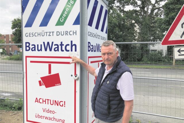 Ein düster dreinblickender Mann zeigt auf ein Schild, das eine Videoüberwachung anzeigt